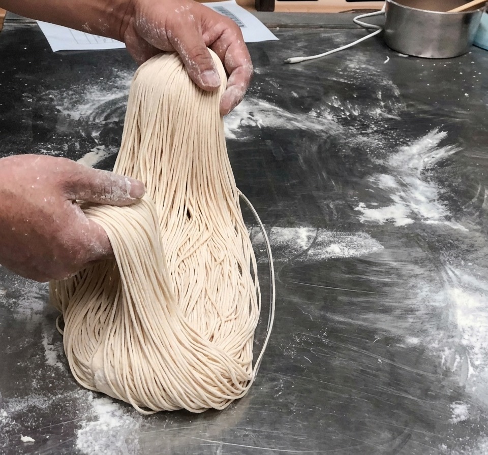 Fili di pasta fresca lunghi e sottili tenuti in aria.