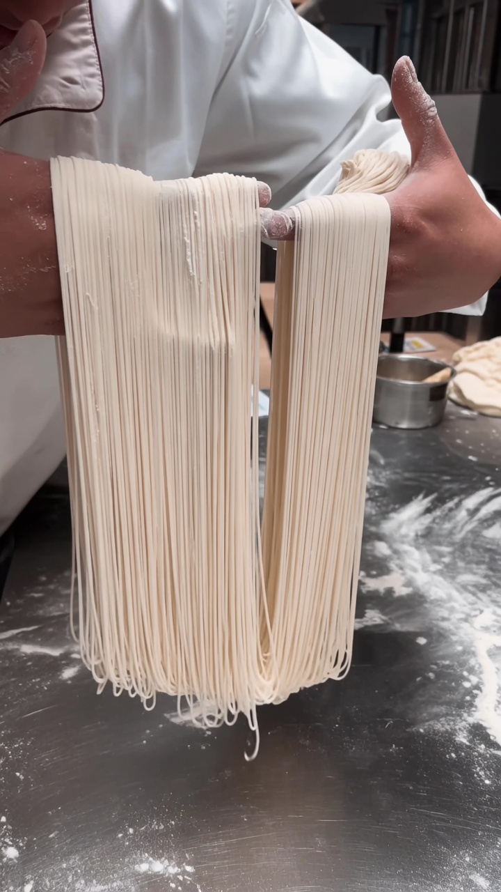 Un grande fascio di noodles tirati, sottili come capelli, sospesi con eleganza tra le mani dello chef.
