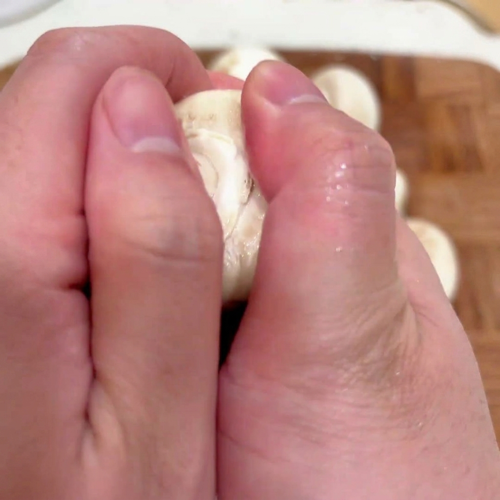 Primo piano delle mani che rimuovono il gambo da una cappella di fungo bianco fresco.