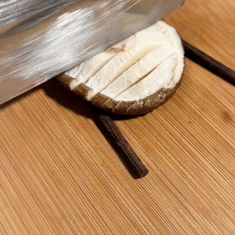 Un coltello che taglia un motivo a croce su un fungo posizionato tra due bacchette.