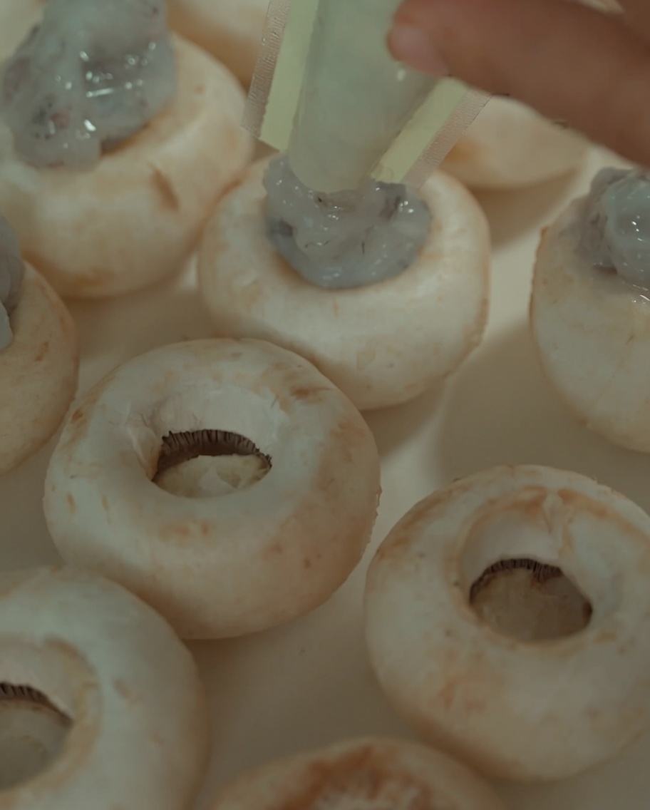 Pasta di gamberi spremuta da un sacchetto nel centro cavo dei funghi cotti.
