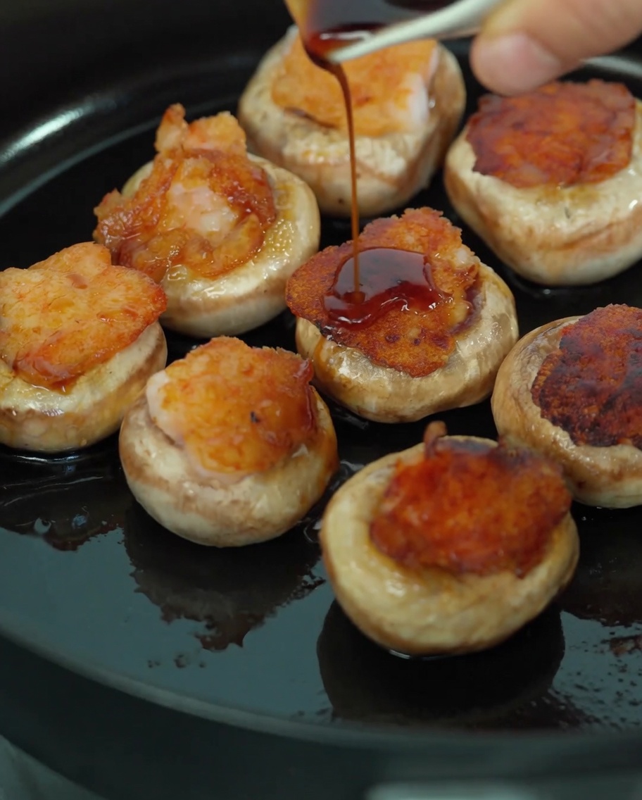 Versare una miscela di salsa di soia e succhi di funghi sopra i funghi ripieni in padella.