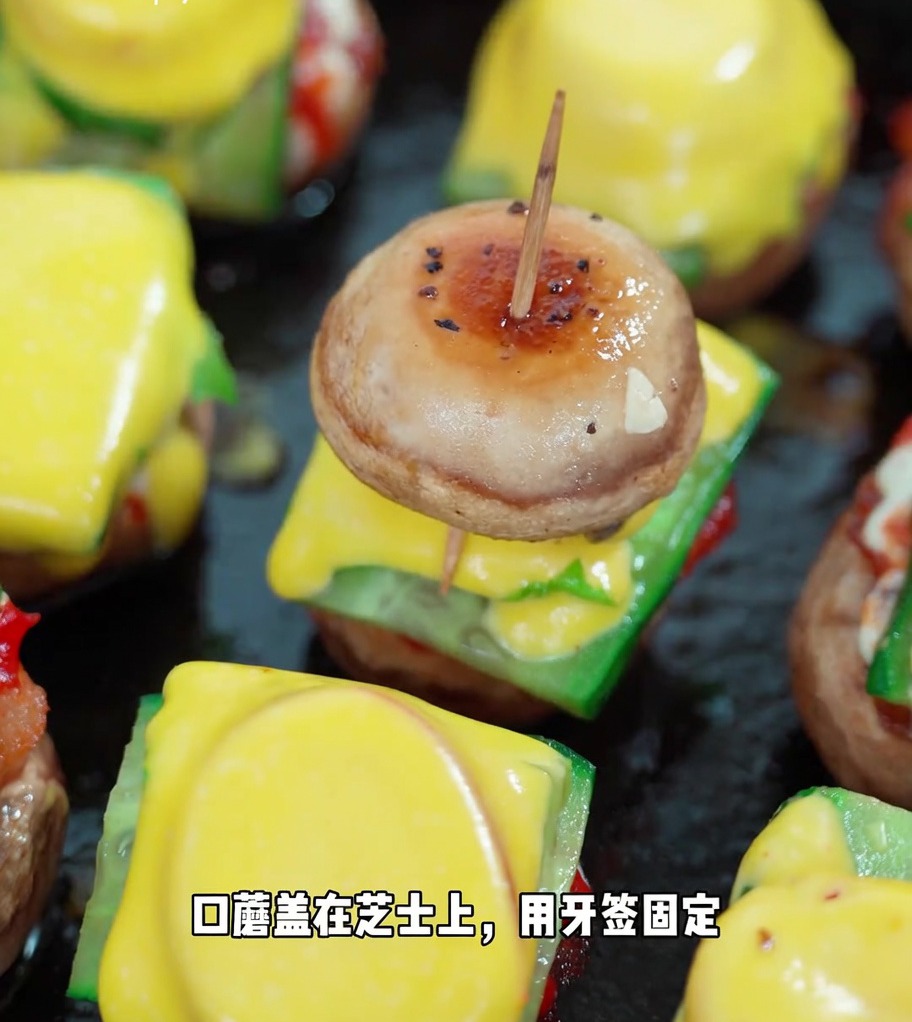 Un mini burger finito fissato con uno stuzzicadenti, mostrando gli strati di fungo, cetriolo, lattuga, pomodoro, formaggio e la seconda cappella di fungo.