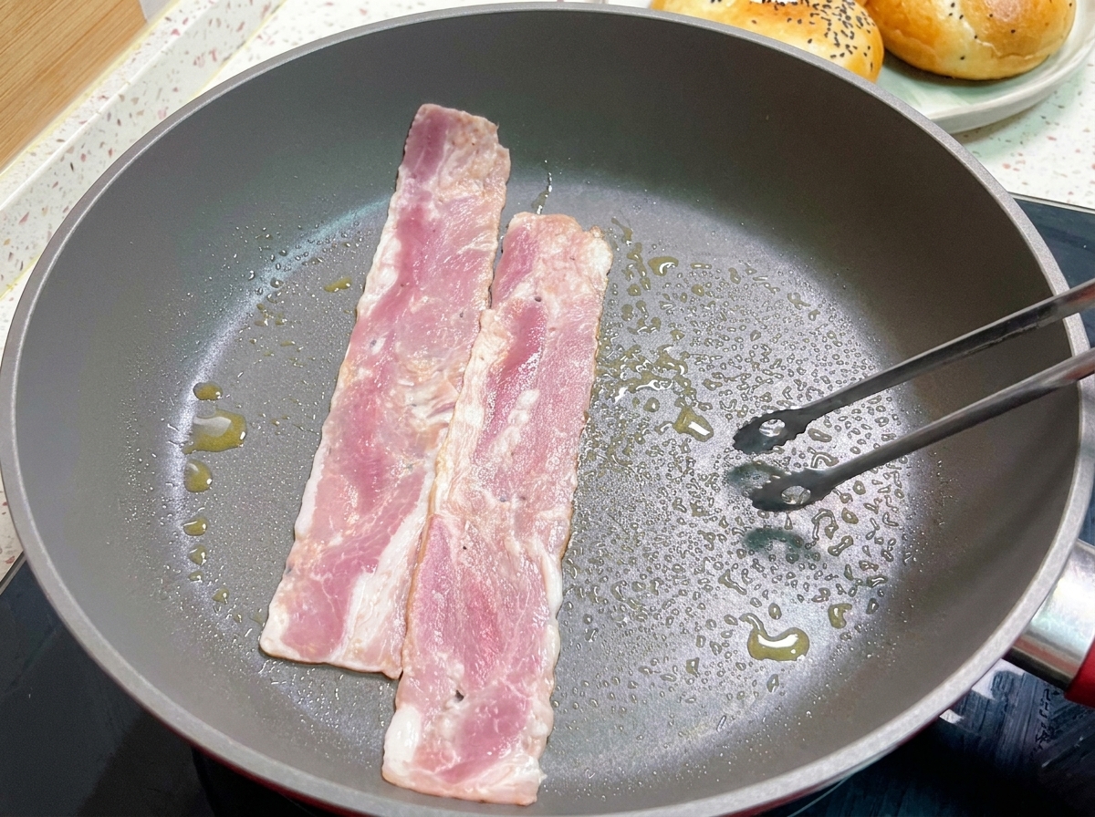 Strisce di bacon che friggono in una padella calda, girate con le pinze.