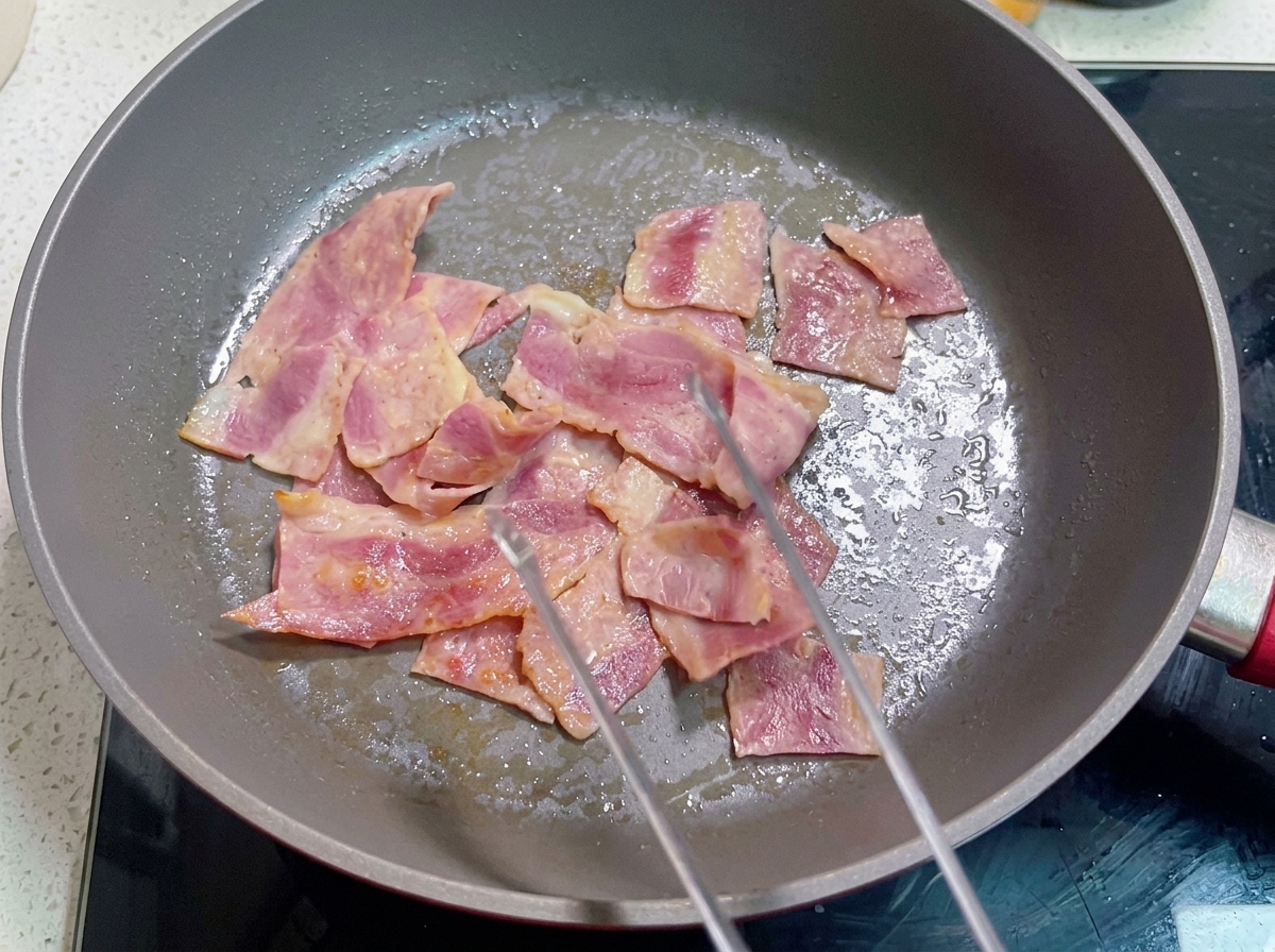 Una padella con bacon cotto su cui viene versato il composto di uova sbattute.