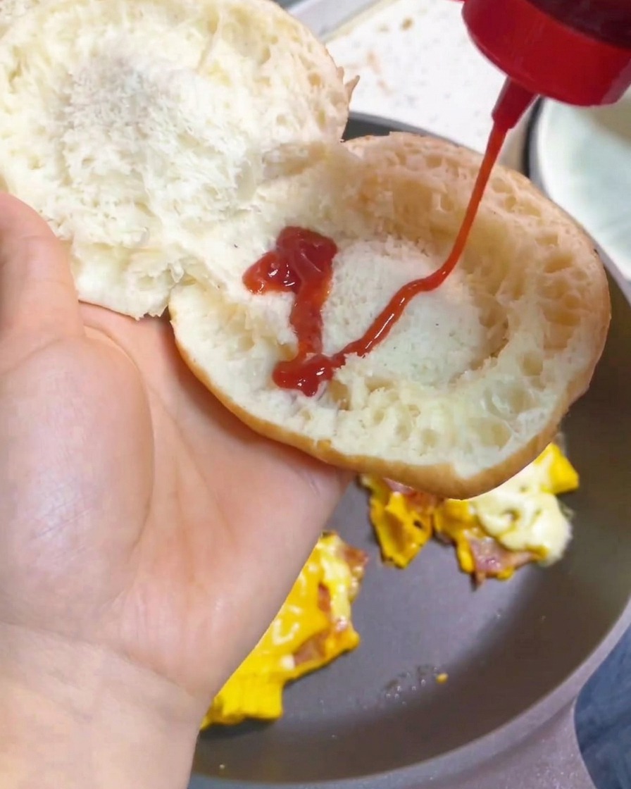 Una mano che distribuisce ketchup a zigzag sullinterno di un panino tostato.