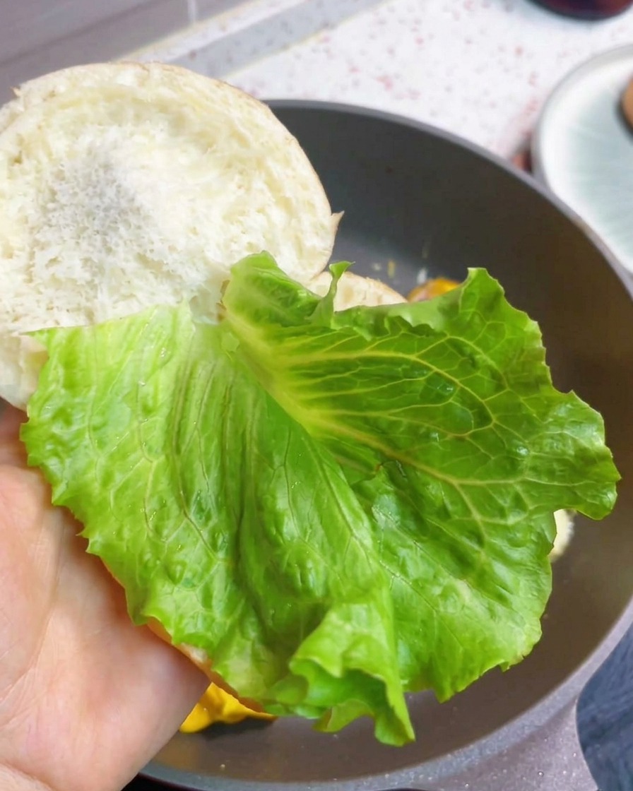 Un burger per la colazione in fase di assemblaggio con lattuga fresca e il tortino di uova, bacon e formaggio.