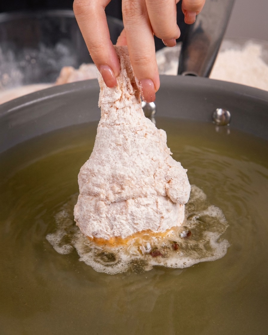Coscia di pollo impanata cruda immersa nellolio caldo in una padella.