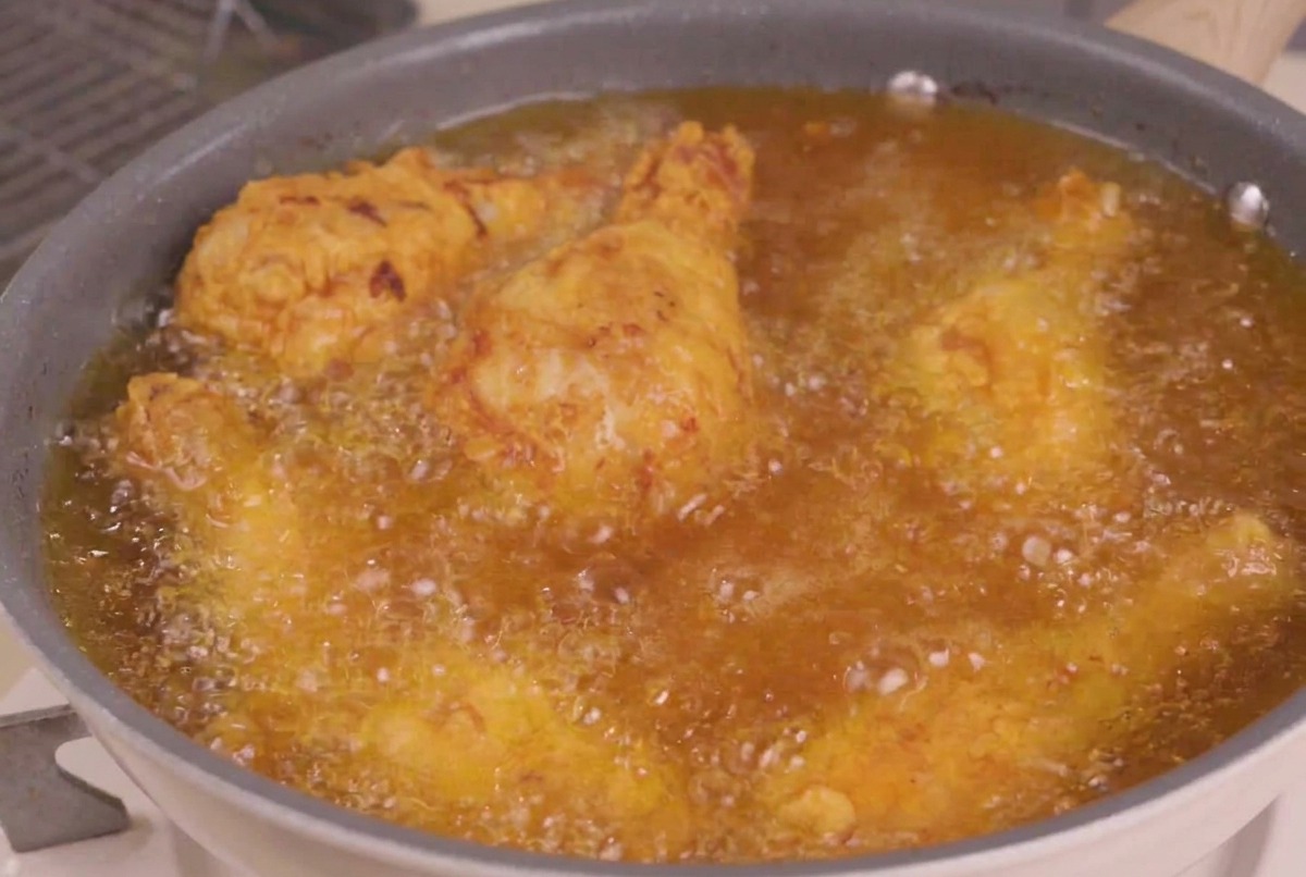 Pezzi di pollo fritto immersi in una padella di olio caldo e frizzante per la fase finale della frittura.