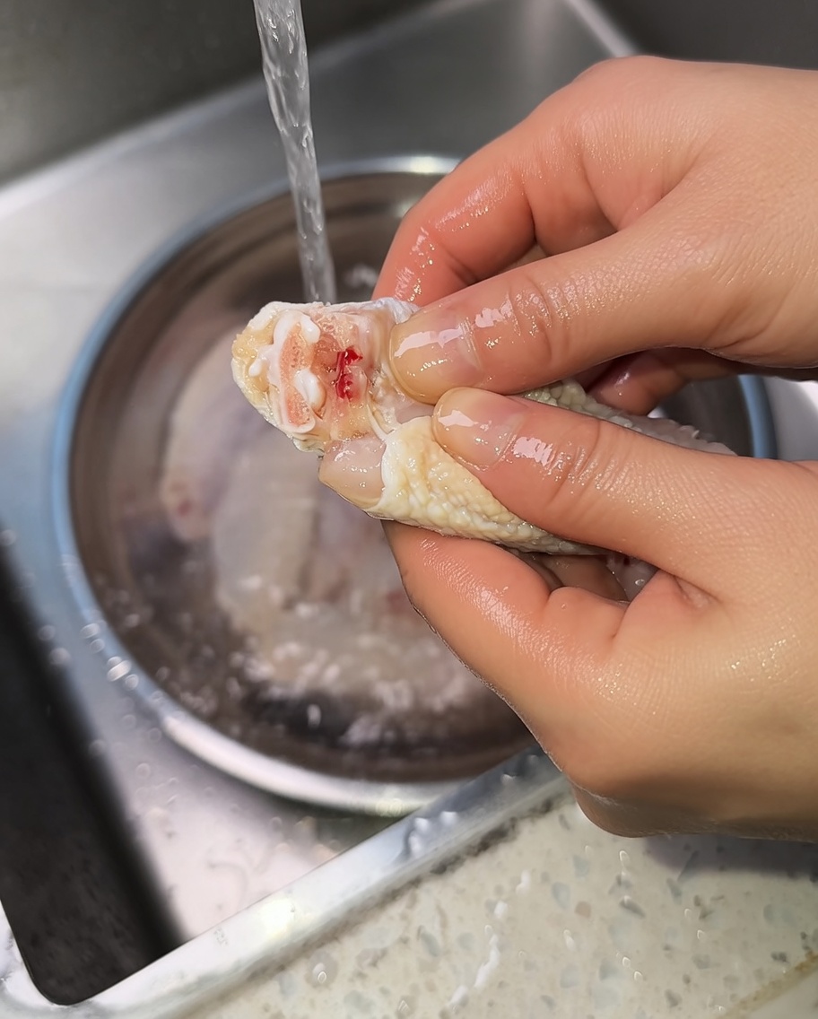 Primo piano delle mani che spremono unaletta di pollo cruda per espellere il sangue dallarticolazione.