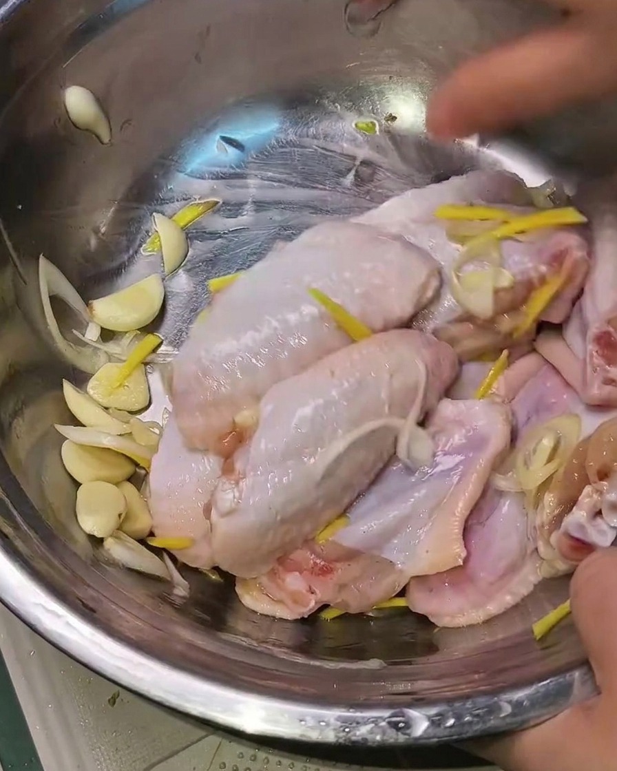 Mani che mescolano le ali di pollo marinate con gli aromi in una ciotola di metallo.