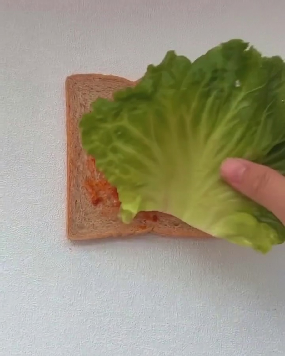 Due grandi foglie di lattuga verde posizionate sopra una fetta di pane già coperta di salsa rossa.
