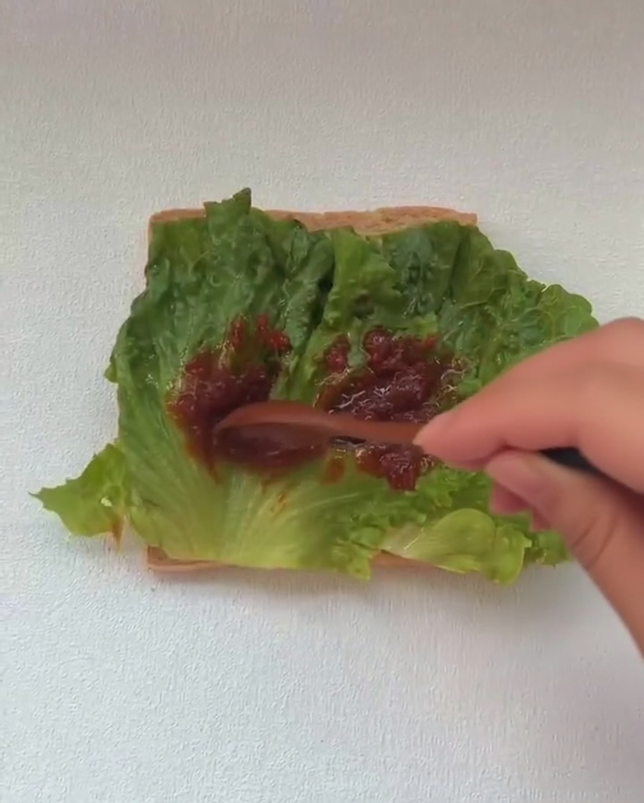 Un uovo fritto appena cotto aggiunto al panino, sopra uno strato di lattuga verde.