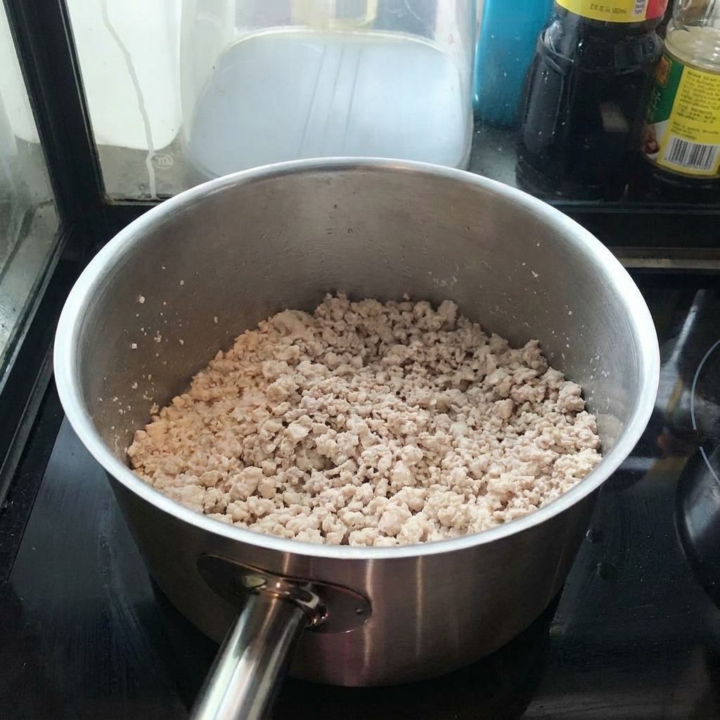 Macinato di maiale che rosola in una pentola, mescolato con una spatola.
