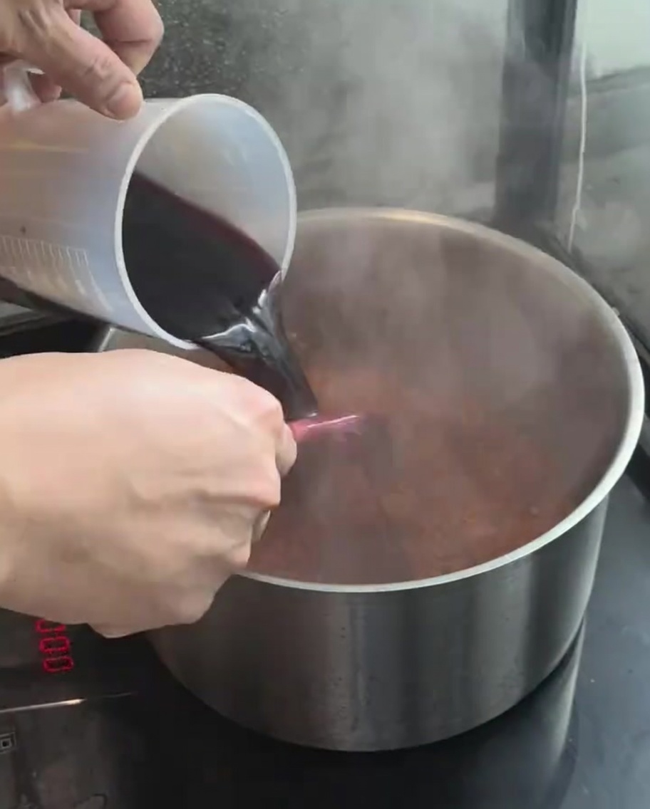Vino rosso versato da un misurino nella pentola con le verdure.