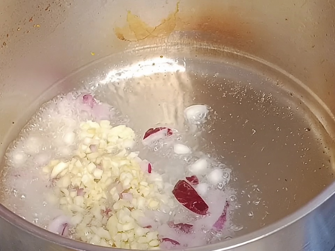 Cipolle rosse tritate e aglio tritato che soffriggono in olio caldo dentro una pentola di metallo.