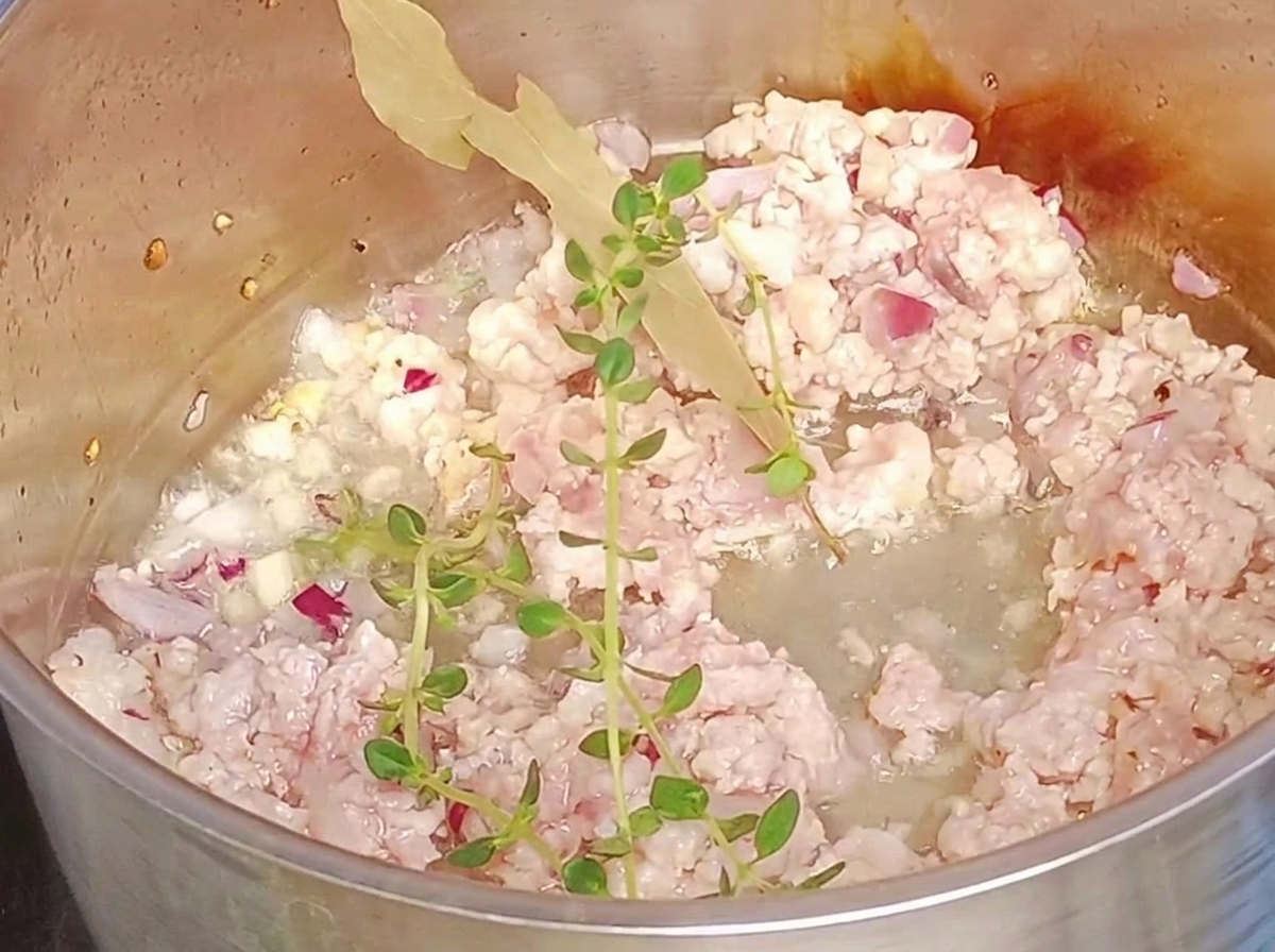 Rametti di timo fresco e una foglia di alloro aggiunti alla carne macinata in una pentola.