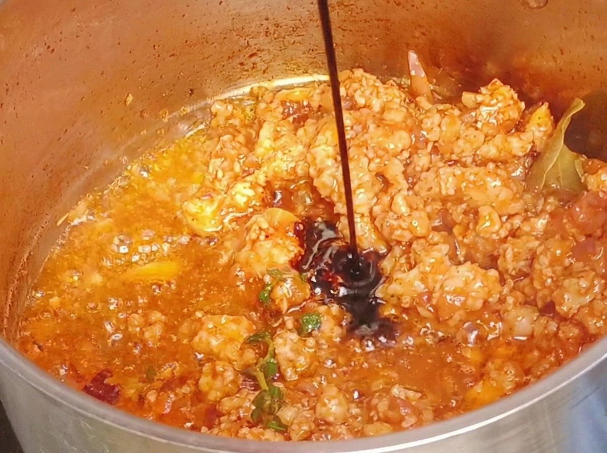 Salsa di soia scura versata in una pentola di carne macinata cotta e rossastra.