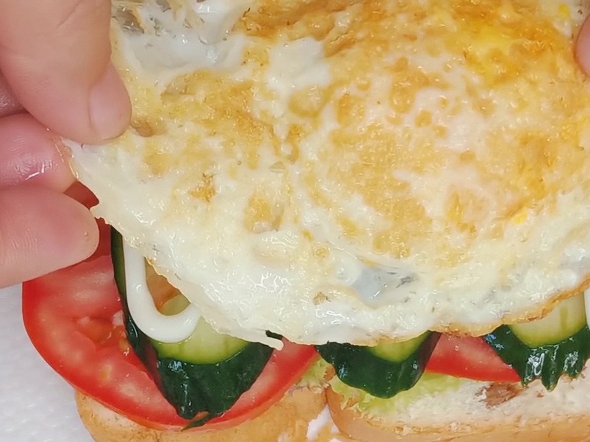 Un uovo fritto perfettamente cotto posizionato sopra gli strati del panino assemblato.