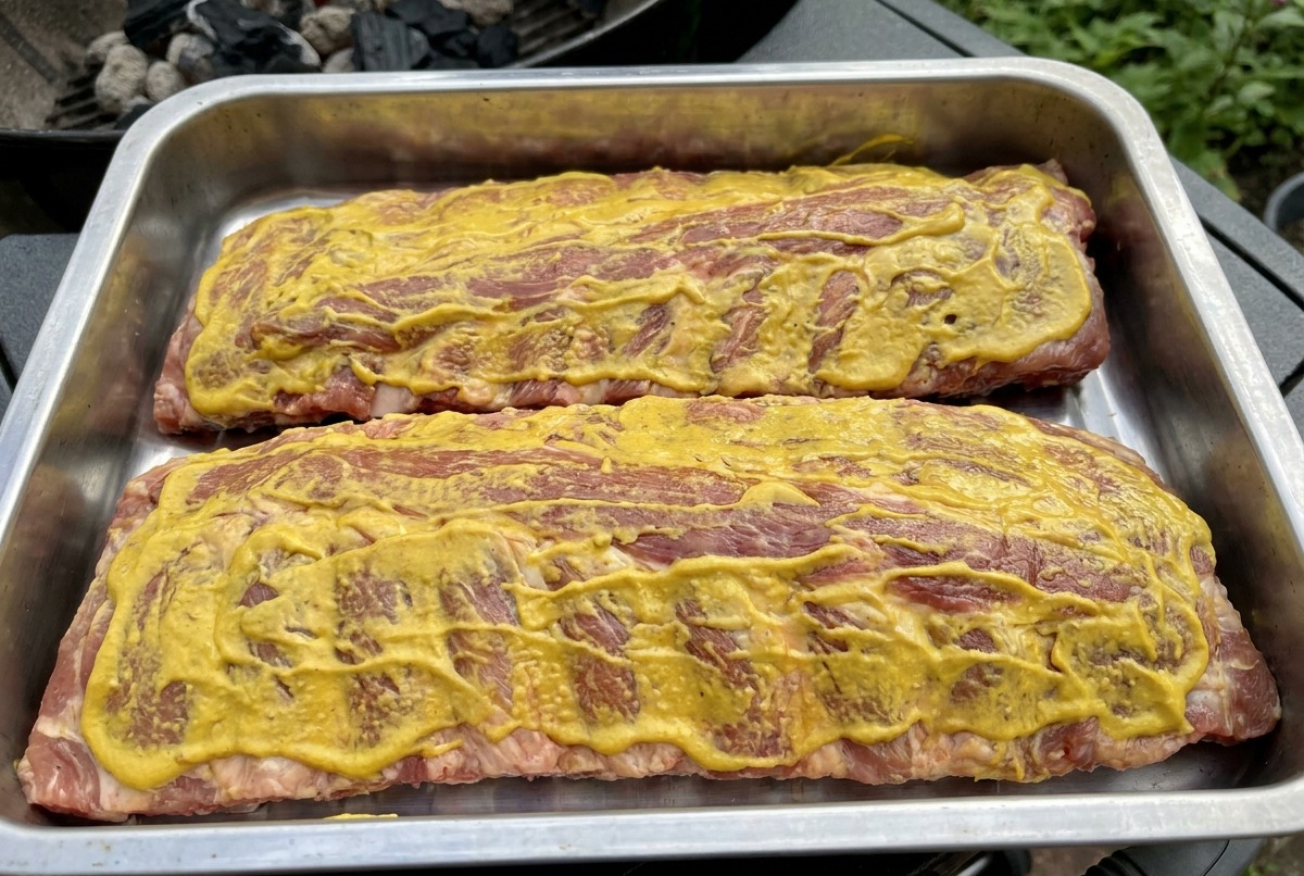 Due rack di costine ricoperte di salsa gialla sulla griglia, pronte per essere affumicate.