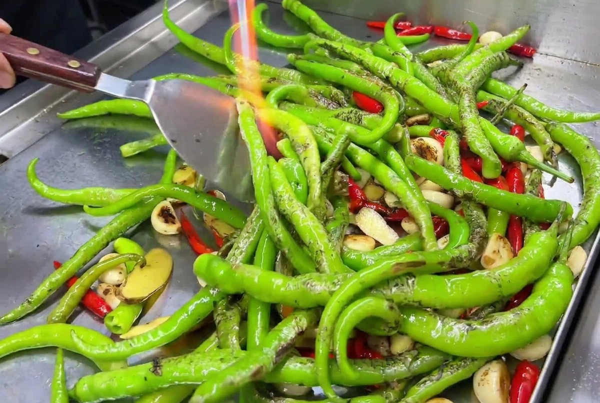 Spicchi daglio e peperoncini rossi rosolati su una piastra calda con la fiamma di un cannello.