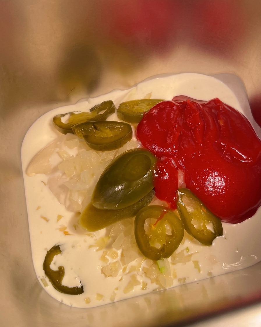 Salsa piccante messicana versata in un contenitore di metallo contenente già la base di panna e maionese.