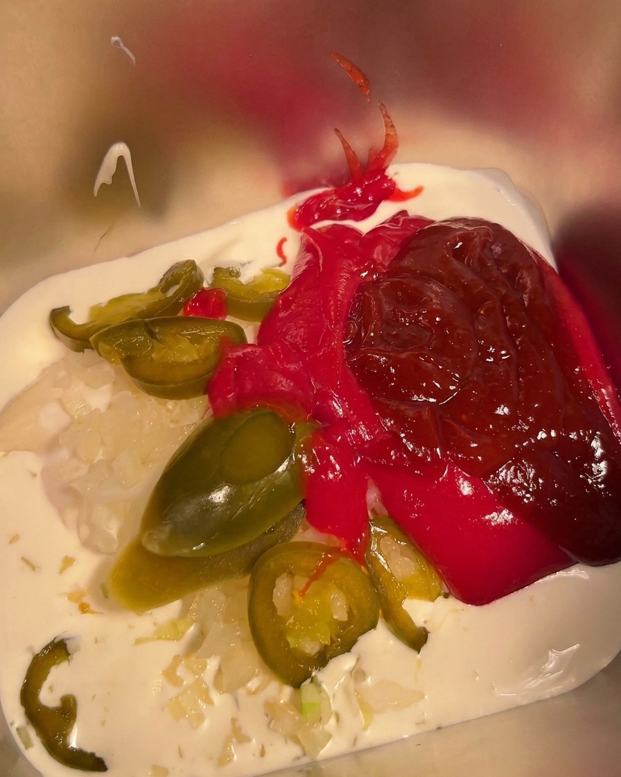 Peperoncino in polvere cosparso sulla miscela di maionese, panna e salsa piccante in un contenitore di metallo.