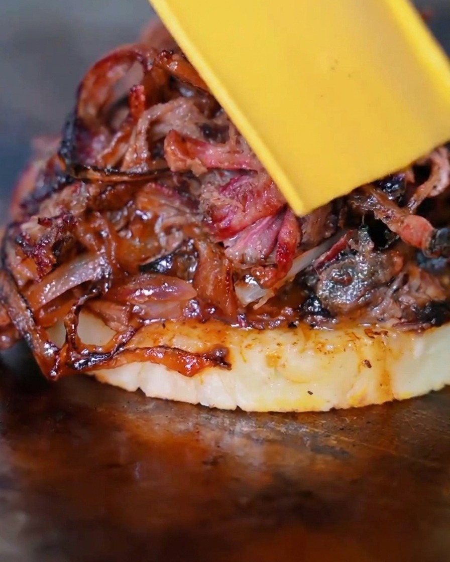 Una fetta di formaggio giallo che si scioglie sopra la pila di manzo, cipolla e ananas.