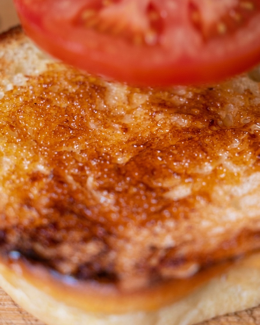 Una fetta di pomodoro fresco viene posizionata sulla metà inferiore del panino tostato.