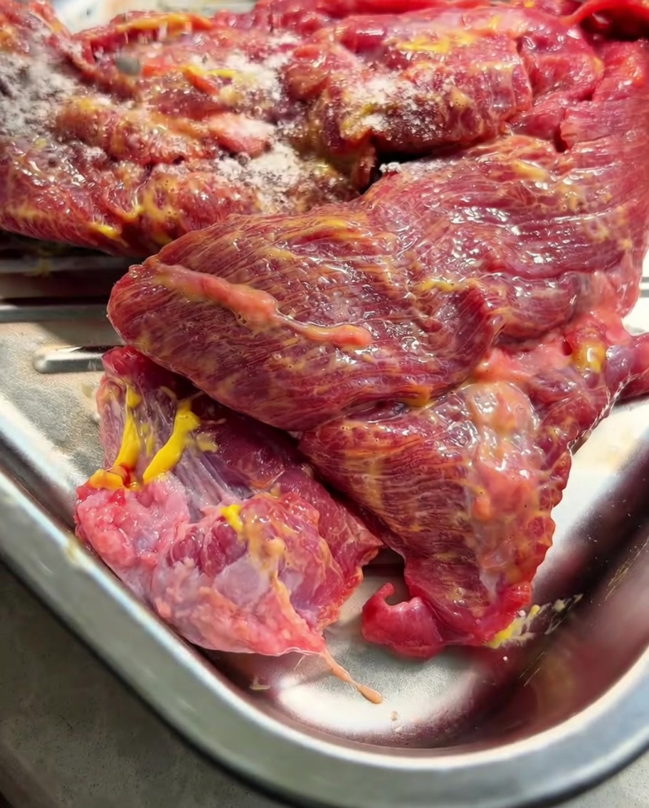 La punta di petto di manzo spalmata di senape su un vassoio di metallo, cosparsa di spezie in polvere sulla parte superiore.