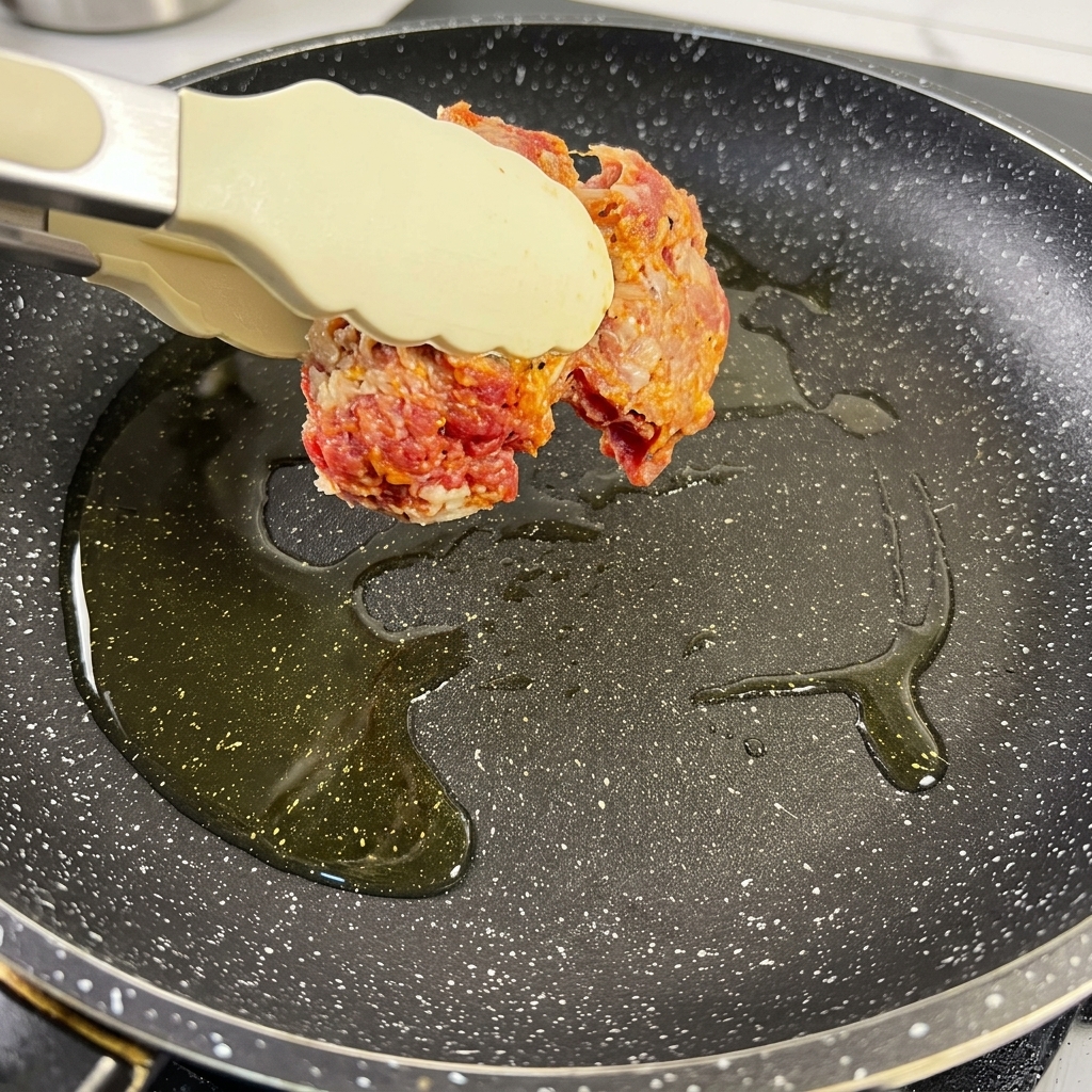 Pezzi di punta di petto di manzo conditi che sfrigolano in una padella calda con olio, diventando di un colore marrone scuro.