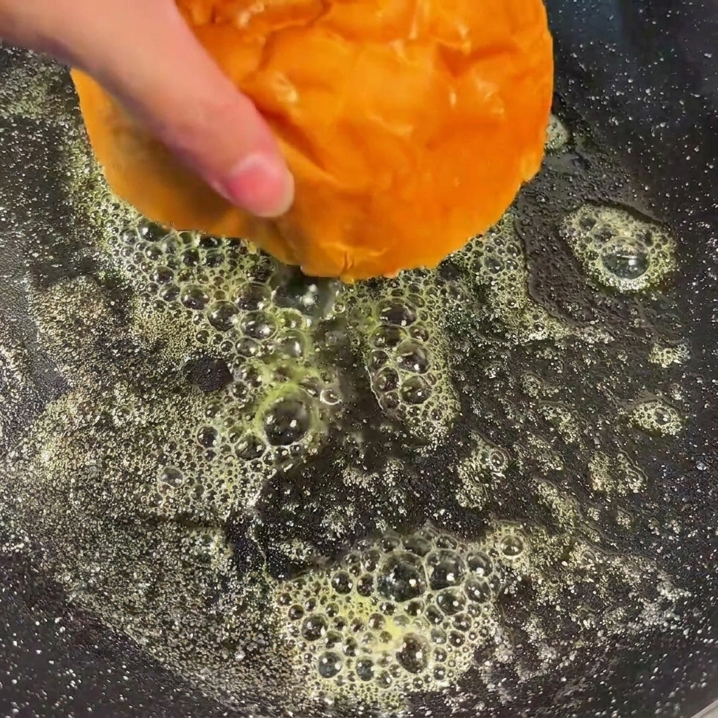 Metà di panini per hamburger rivolte verso il basso in una padella con burro fuso, che si tostano fino a diventare dorate.