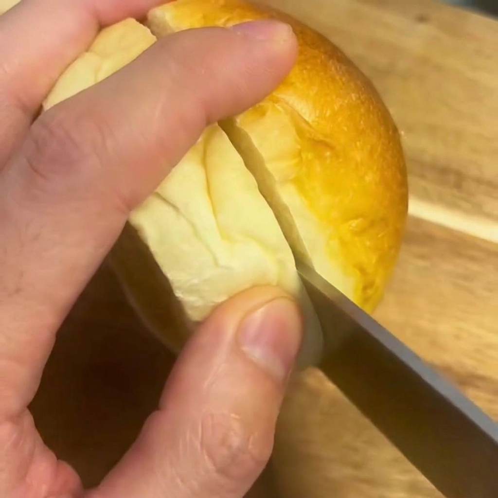 Un coltello che taglia a metà un morbido pane per hamburger su un tagliere di legno.