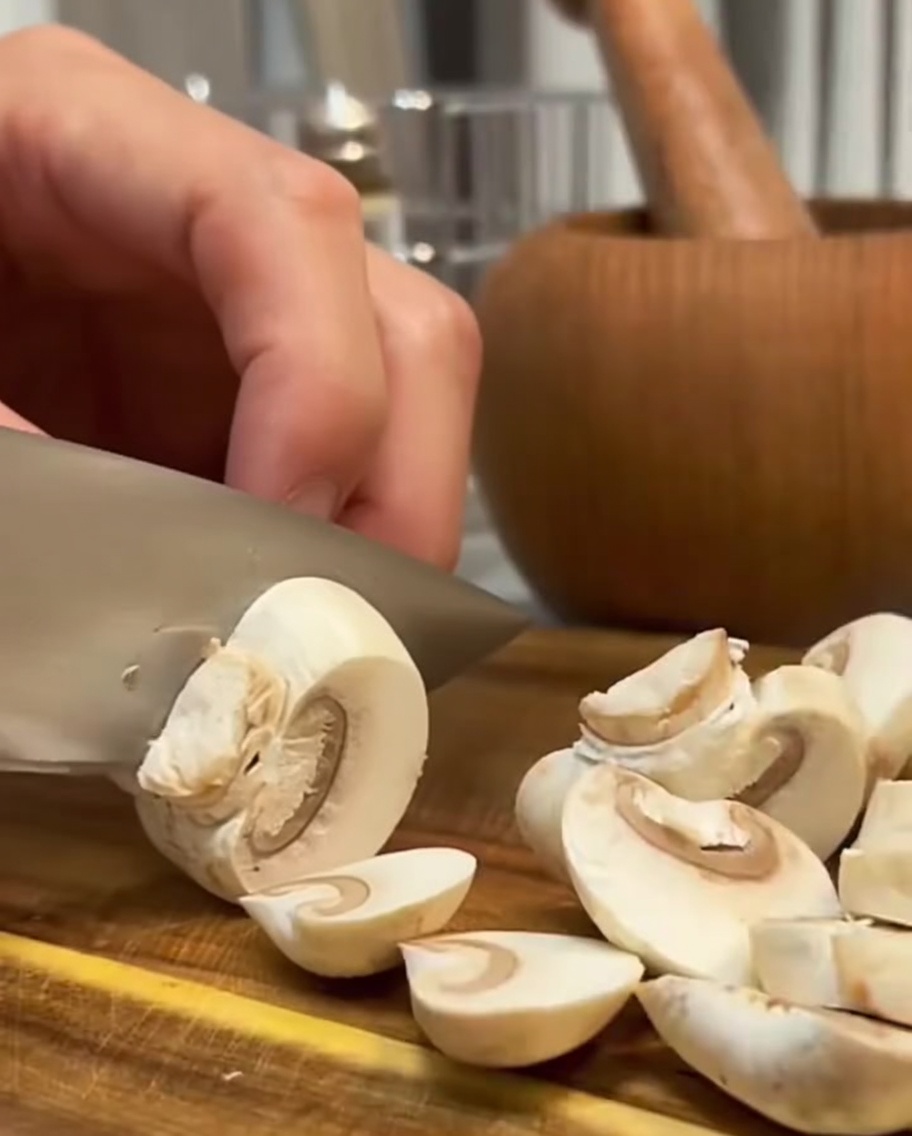 Funghi freschi tagliati a fette con un coltello su una superficie di legno.