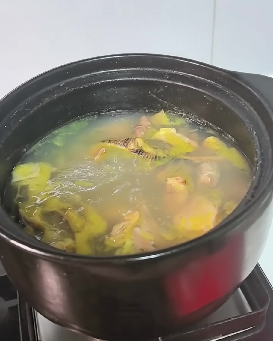 Una pentola nera di brodo di pollo che sobbolle sul fornello.