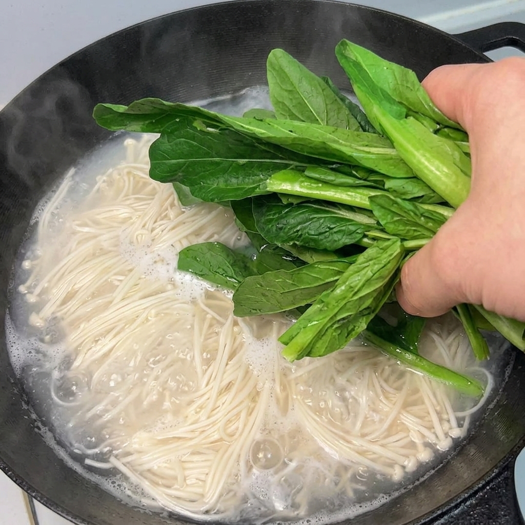Verdure a foglia verde aggiunte a una pentola di noodles bollenti.