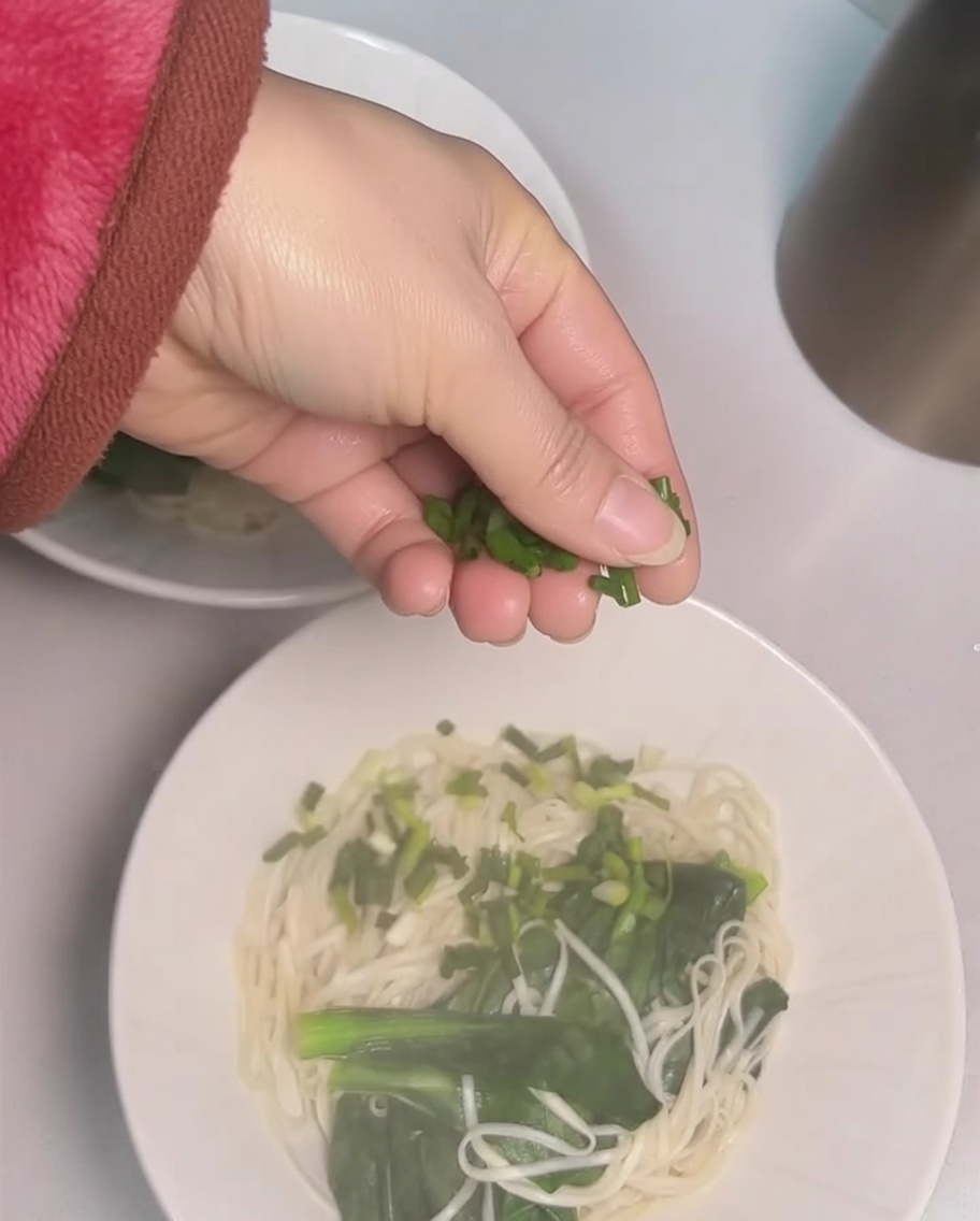 Mano che sparge cipollotti tritati su una ciotola di noodles.