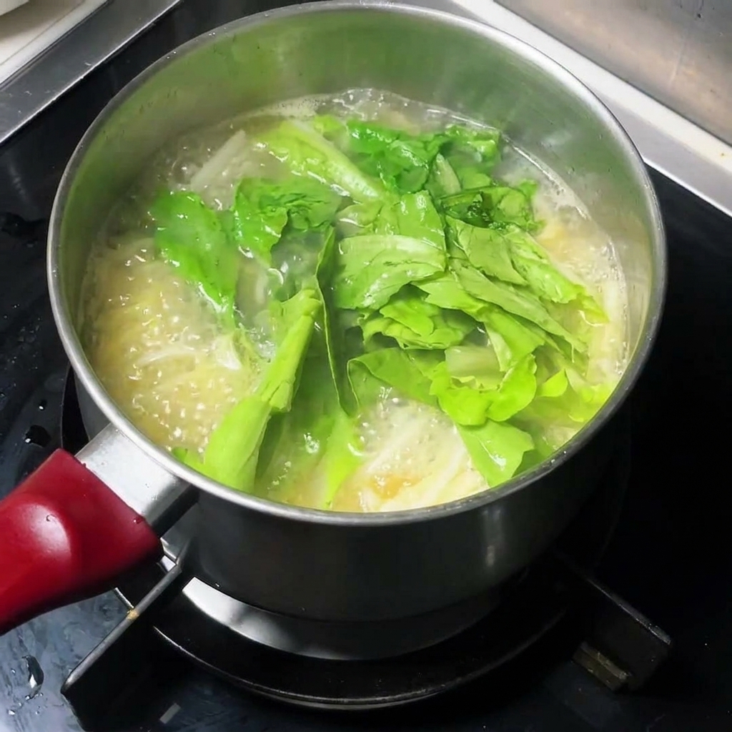 Verdure a foglia verde fresca aggiunte a una pentola di zuppa di noodles bollente.