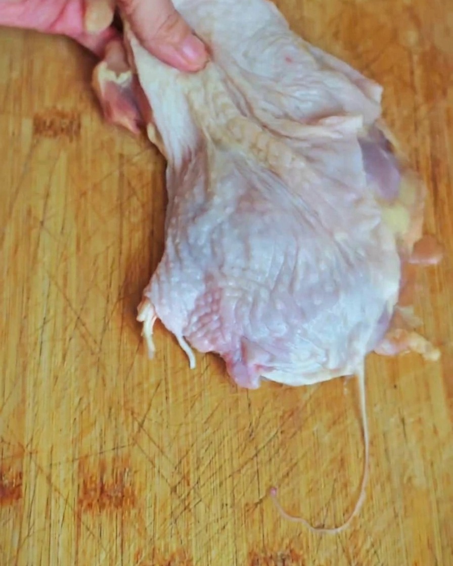 Un primo piano di carne di coscia di pollo tagliata a pezzetti su un tagliere di legno.