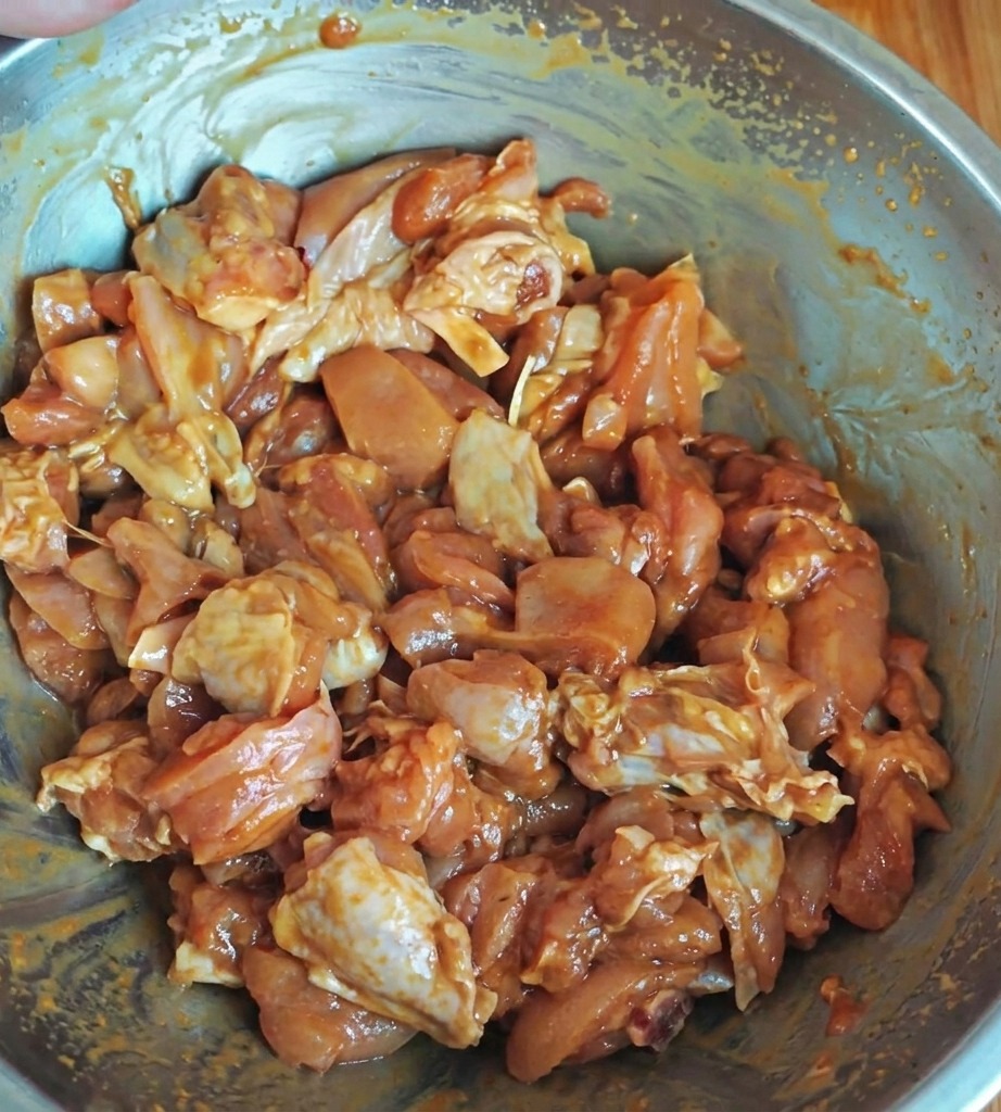 Pezzi di pollo conditi che marinano in una ciotola di metallo, ricoperti da una miscela di salsa lucida.