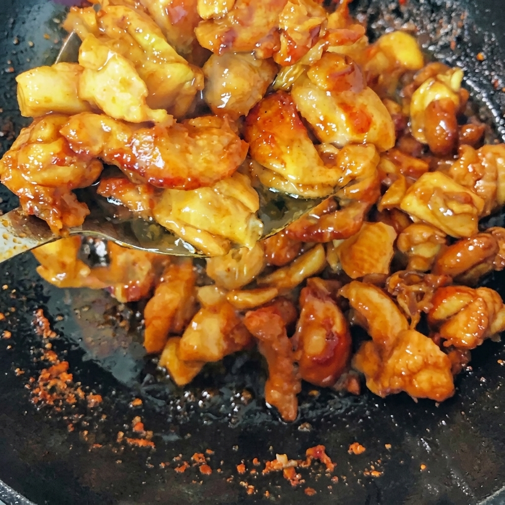 Pezzi di pollo rosolati che saltano in un wok con cipollotti, fette di zenzero e peperoncini secchi.