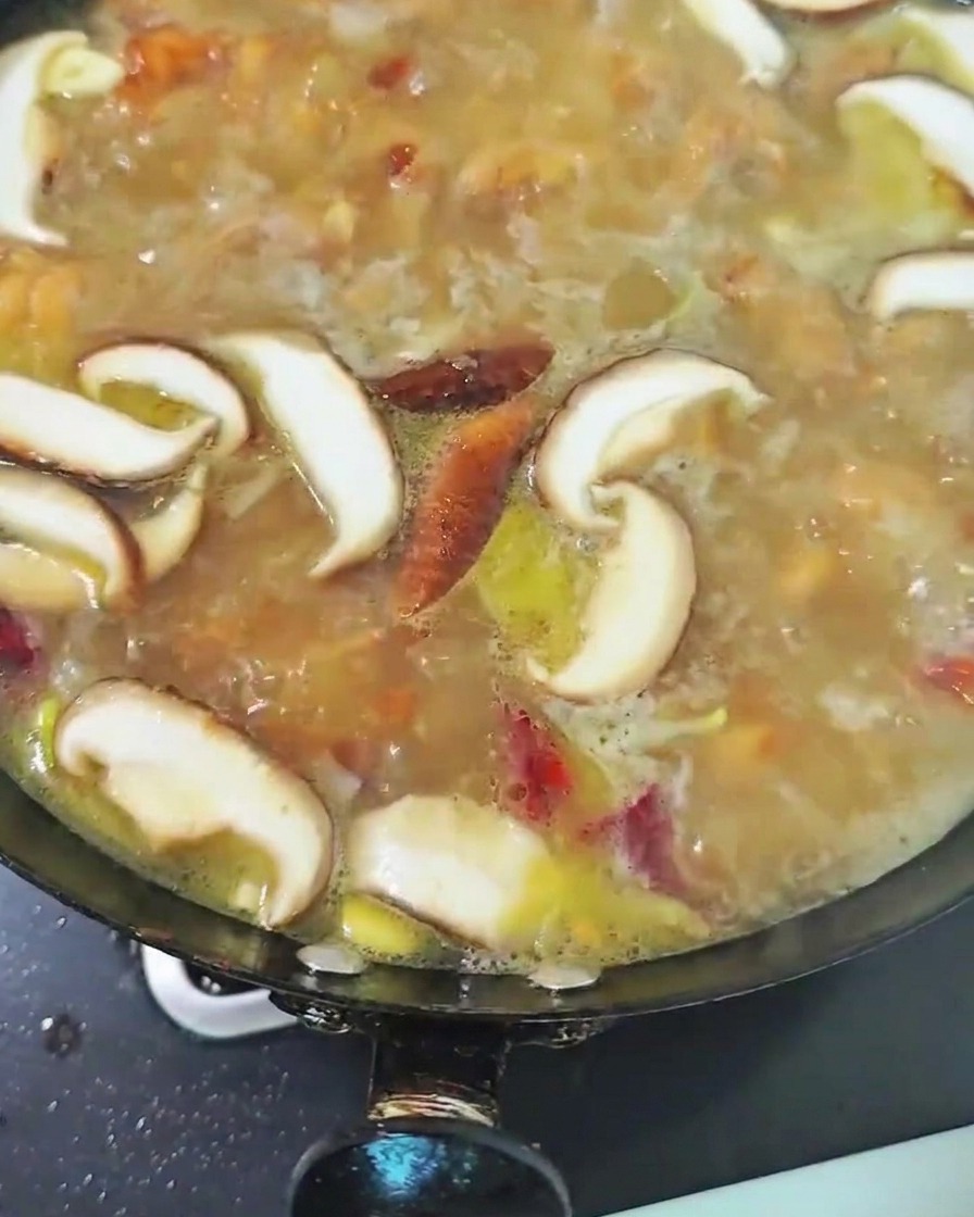 Funghi shiitake affettati che sobbollono nel brodo di pollo allinterno del wok.