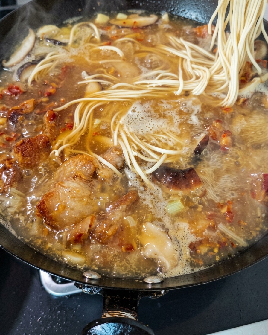 Noodles freschi che vengono immersi in un ricco brodo gorgogliante di pollo e funghi in un wok.