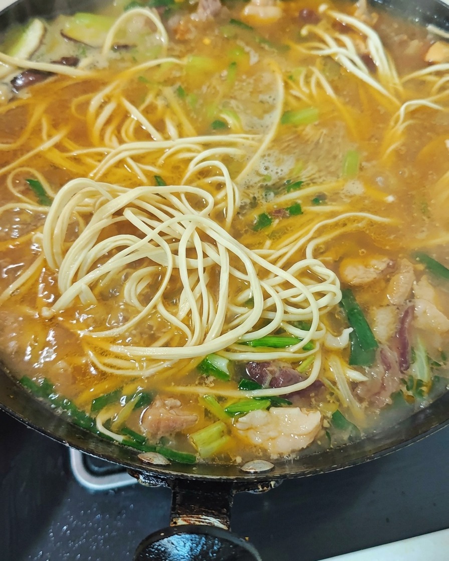 Verdure verdi e germogli daglio tritati mescolati nella zuppa di noodles bollente.
