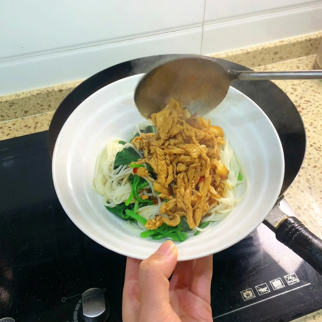Un mestolo che versa una porzione abbondante di pollo e tofu brasato sopra una ciotola di noodles.