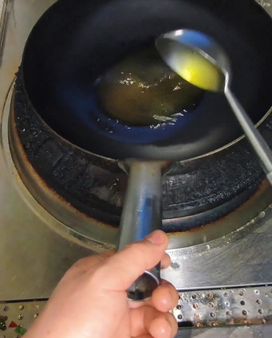 Un mestolo di metallo versa olio di cottura in un wok caldo.