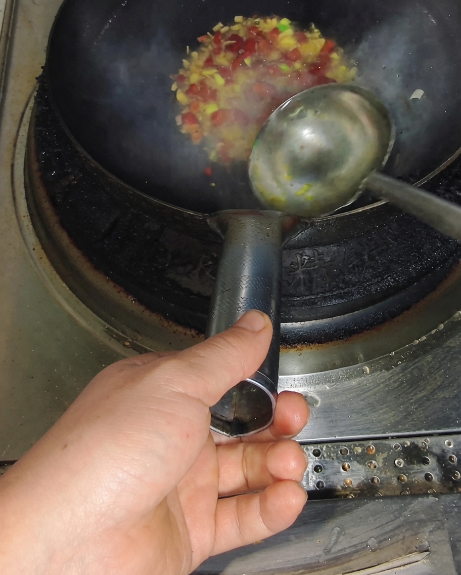 Brodo versato nel wok con aromi che sprigiona vapore.