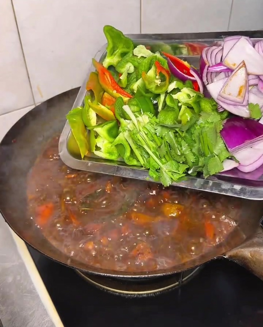 Peperoni freschi, cipolle e coriandolo aggiunti al wok durante la cottura.