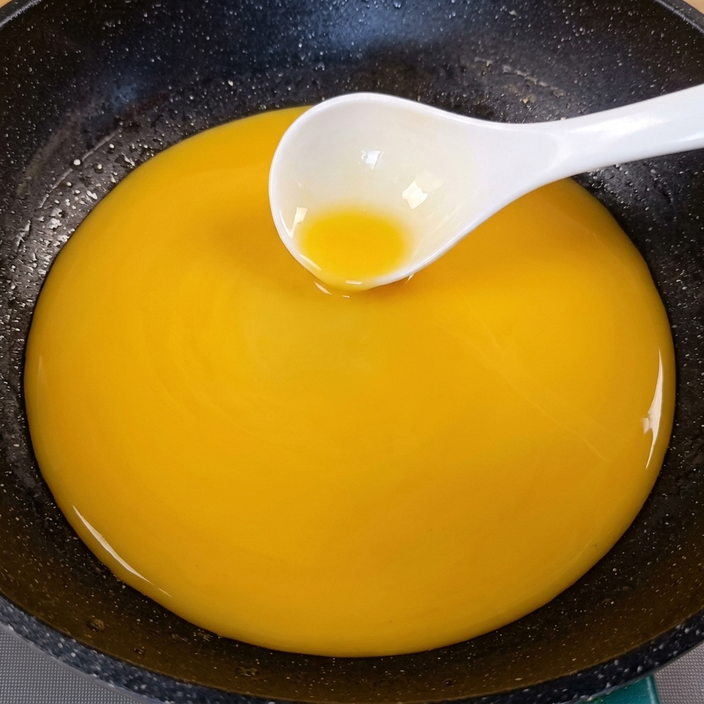 Una salsa giallo dorata densa mescolata in una padella scura con un mestolo bianco.