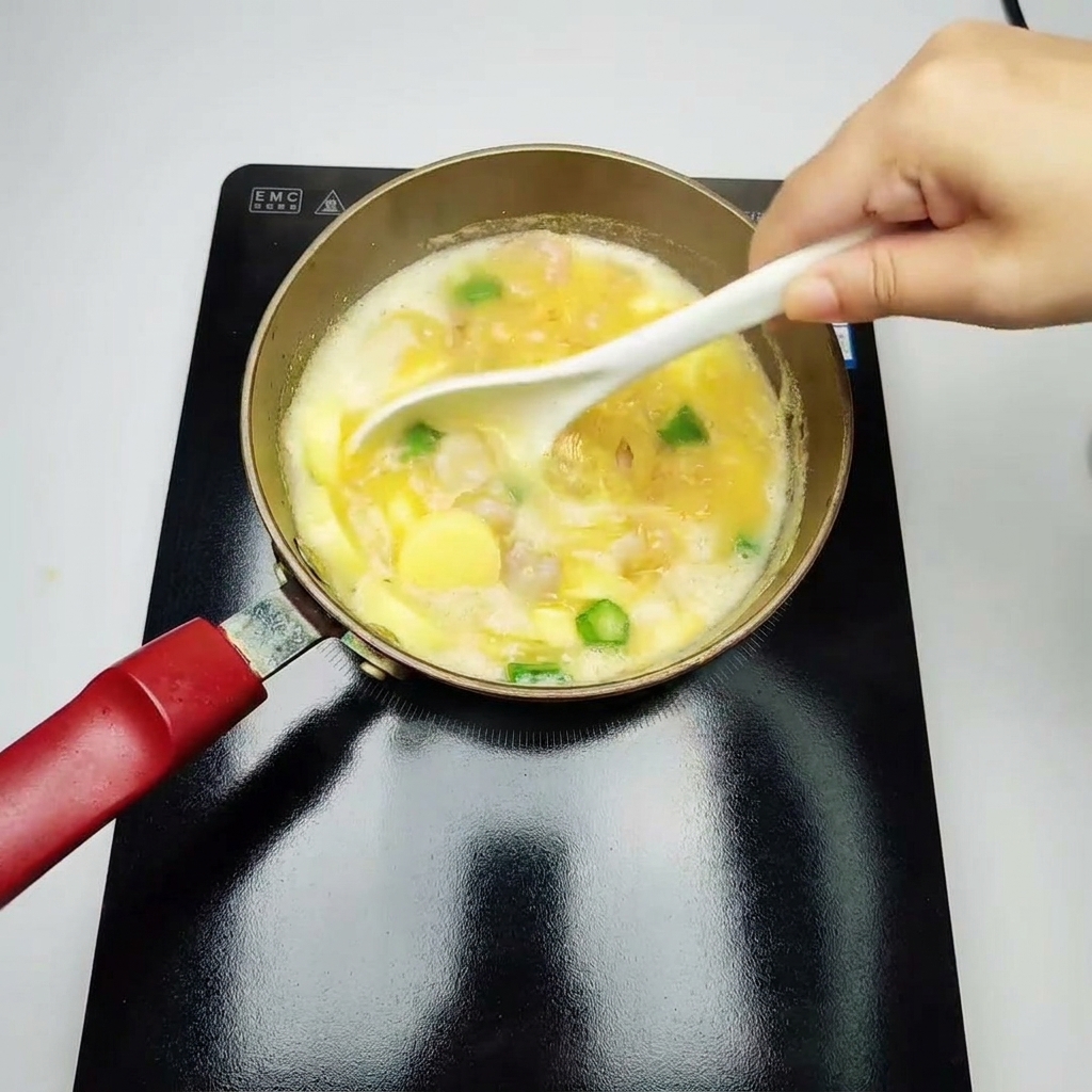 Un mestolo bianco che mescola delicatamente una zuppa gialla a fuoco lento, piena di gamberi cotti, pezzi di gombo verde e tofu alluovo a fette.